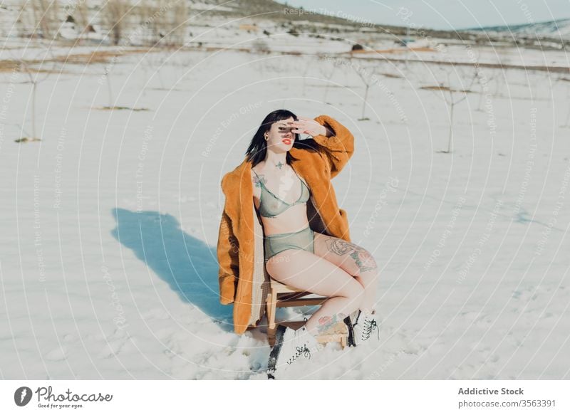 Young woman in fur coat and lingerie sitting in snowy field sensual nature winter brunette confident female trendy young slim style fashion lady attractive