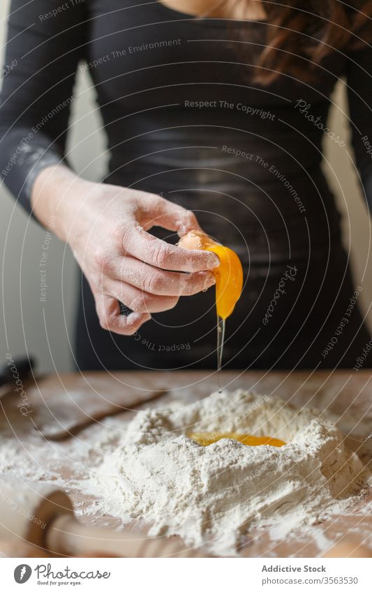 Crop housewife adding eggs to flour while making dough raw break woman kitchen cook pastry prepare rolling pin ingredient process homemade table pasta food