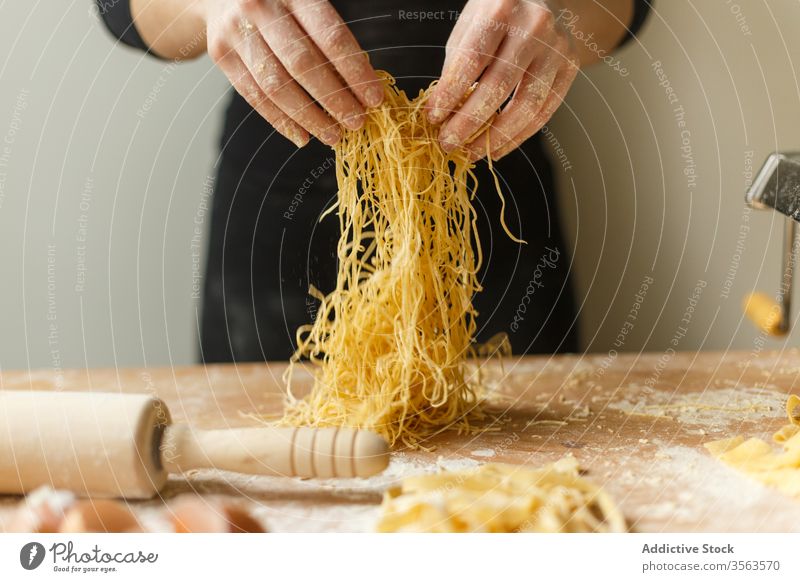 Unrecognizable woman with cut raw pasta homemade dough strap thin stripe pastry cook table flour kitchenware roll eggshell prepare ingredient process