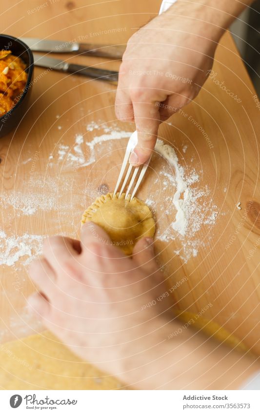 Crop person making ravioli on table press fork bowl dough cook pastry flour process prepare kitchen food cuisine knife kitchenware culinary homemade recipe