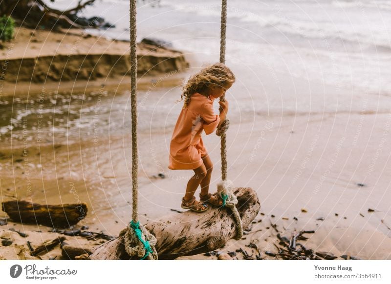 Girl stands on a swing and swings towards the sea Hawaii Hibiscus To swing Rocking Joy Playing Exterior shot Colour photo Swing Playground Infancy Day Child
