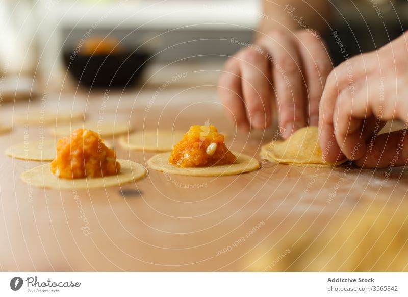 Crop person stuffing ravioli with pumpkin filling dough prepare circle cook table round wooden process kitchen food cuisine culinary homemade dish recipe