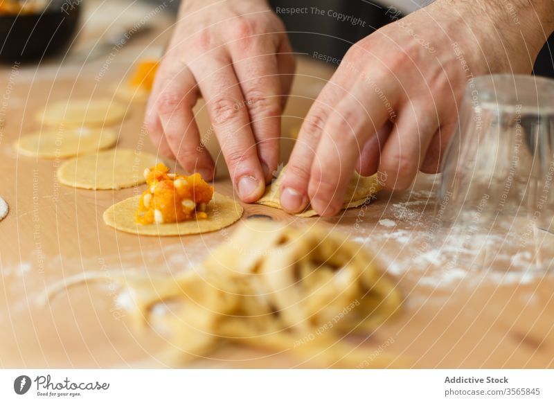 Crop person stuffing ravioli with pumpkin filling dough prepare circle cook table round wooden process kitchen food cuisine culinary homemade dish recipe