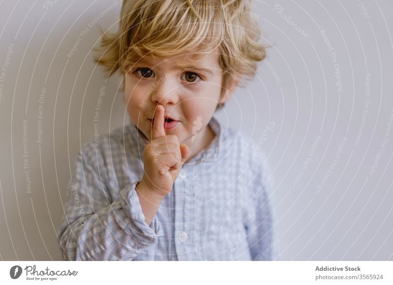 Adorable boy making silence gesture adorable index finger gesticulate little cute kid child content childhood casual face expression happy stand touch lips