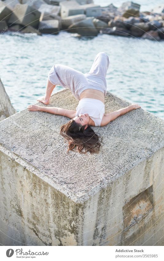 Young woman lying on stone construction near sea shore breakwater sensual dancer concrete contemporary concept modern allure body enjoy young female seaside