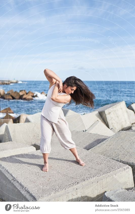 Modern woman standing on concrete block of breakwater sea dance sensual power harmony coast contemporary concept stone construction energy physical young pose