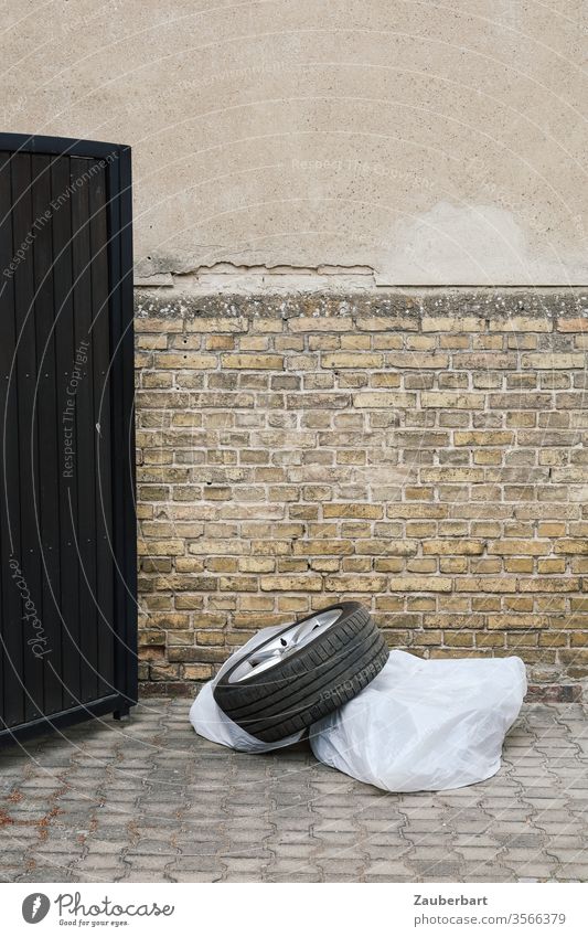 Tire on rim, plastic cover, door and wall in yellow-brown and light gray Car tire Wheel rim Plastic bag Wall (building) brick bailer pavement Gray Gloomy Brown