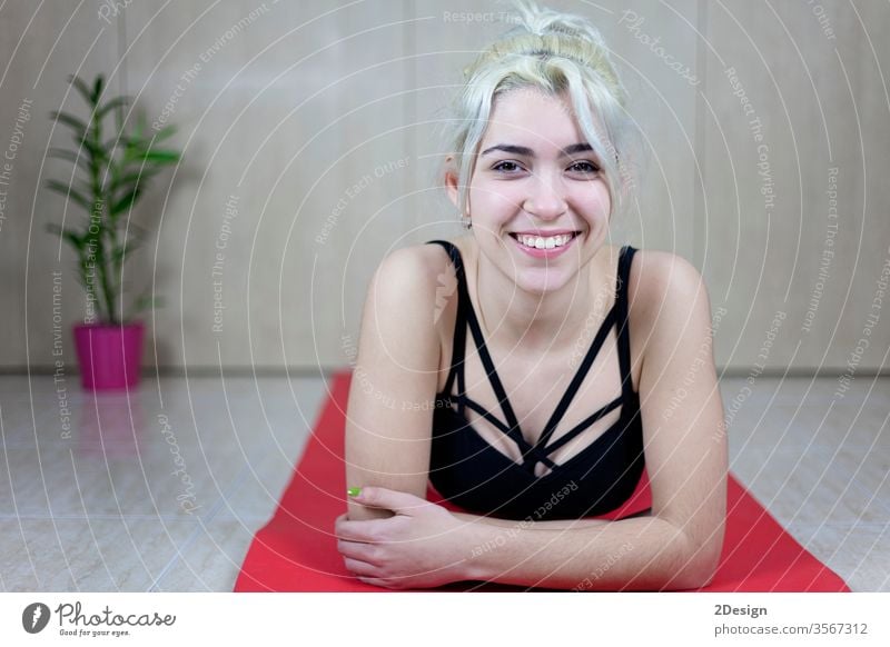 Front view of a smiling beautiful young woman arms crossed lying on a yoga mat while looking camera person indoor adult female lifestyle body caucasian fitness