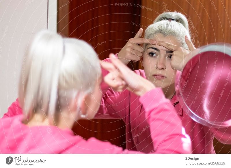woman in bathrobe looking at pimple on face into the mirror and try to squeeze it. person beauty acne skin care female adult young girl problem touching