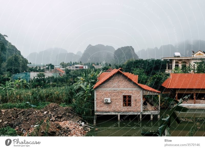 Landscape with houses in Vietnam foggy Ninh Binh Water stilts Green South East Asia Limestone rocks roofs Village