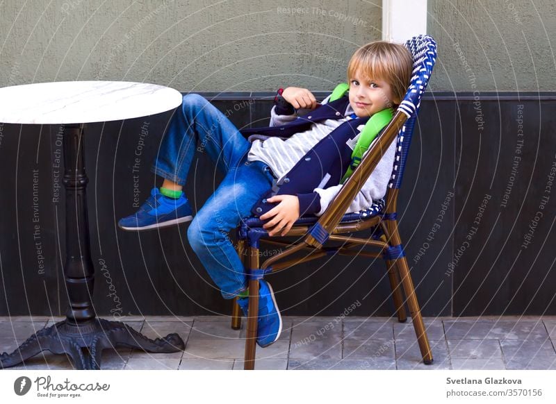 The boy sits on a chair in a city cafe. young in cafe sitting at cafe people coffee table hipsters restaurant family eating food restaurant child cute street