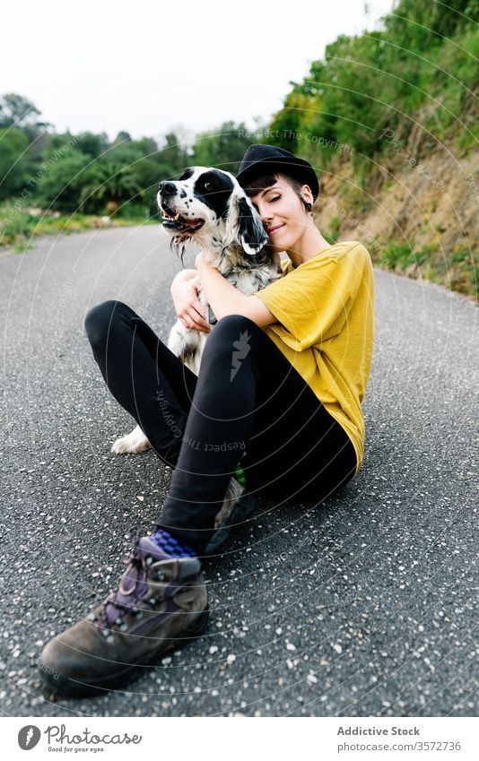 Cheerful young lady sitting on ground with her dog woman cheerful walk fun park nature hipster subculture style together companion street hat pet leisure relax