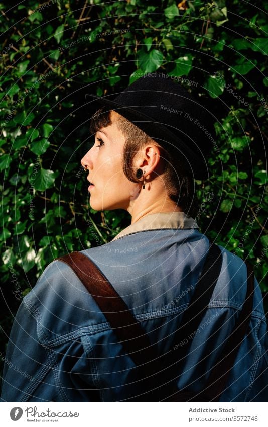 Stylish young lady in hat standing near blooming bush on street woman back view positive hipster nature style subculture charming human face portrait blossom