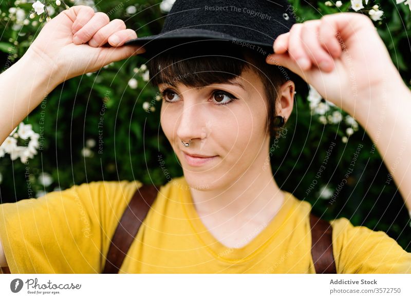 Stylish young lady in hat standing near blooming bush on street woman positive hipster nature style subculture charming human face portrait blossom beautiful