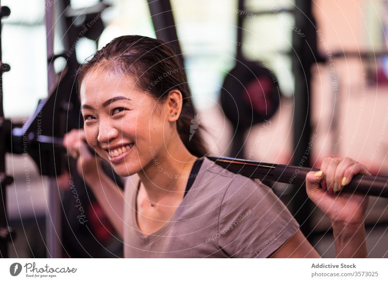 Powerful young Asian sportswoman doing squat with barbell in modern gym workout active wear machine equipment focus asian breathe smile happy strong athlete
