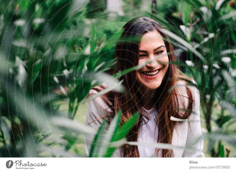 Young pretty woman laughs heartily amidst green plants outside in the garden Woman youthful Laughter Joie de vivre (Vitality) Nature fun portrait luck Happiness