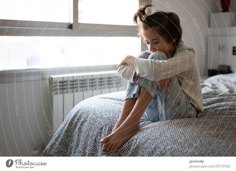 Nine-year-old girl sitting in bed bored by confinement morning lock down sad quarantine thoughtful room seclusion self isolation temperature daughter stay home