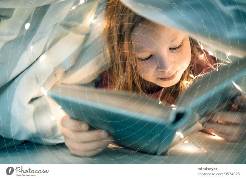 Girl reads book under the covers girl Child portrait Reading Book Bed Duvet Fairy lights Infancy underhand covert thrilling Colour photo Study Interior shot