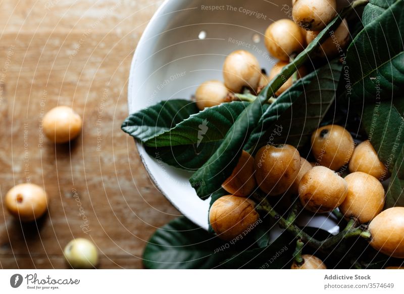 Fresh branch of loquat fruits on table nispero healthy food white ceramic plate wooden shabby fresh green leaf desk rustic rural style aged surface organic