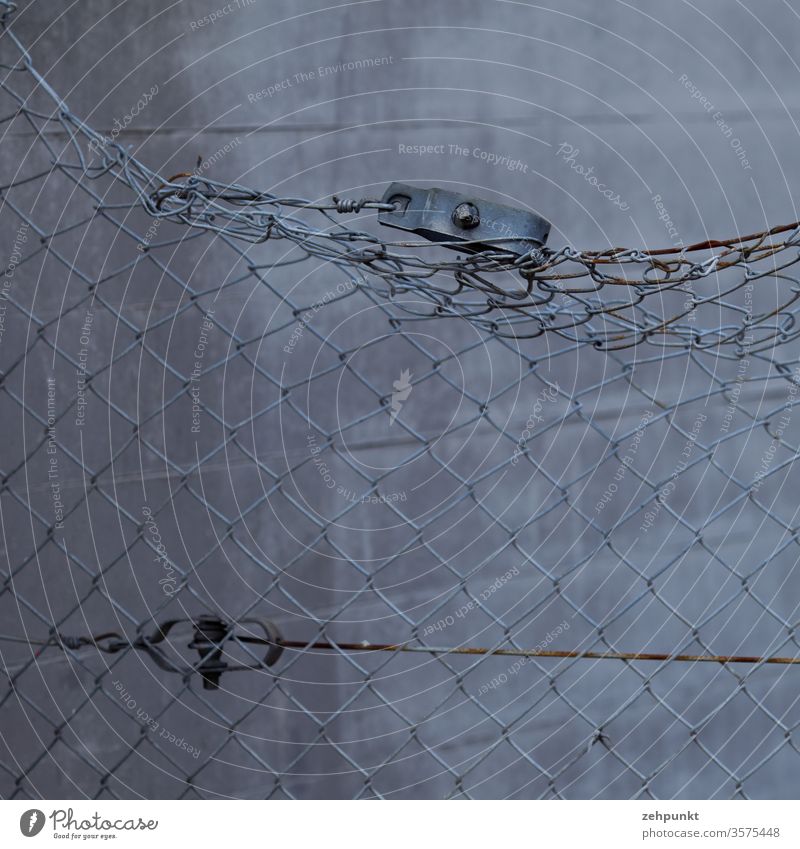 A bent wire mesh fence in front of a grey concrete wall Wire netting fence Fence warped Concrete wall Rust top Gray Grid