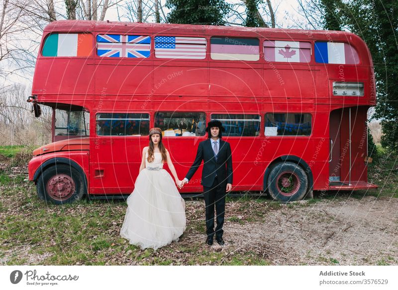 Newlywed couple near red bus in forest newlywed wedding elegant double decker bride groom holding hands love dress suit leather jacket shabby retro vintage