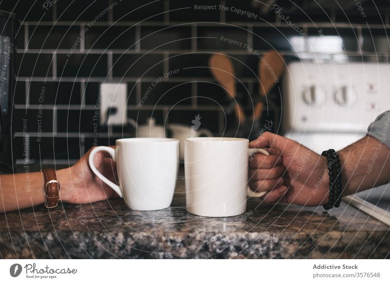 Crop unrecognizable couple taking cups of hot drink in kitchen hand take together relationship table marble wristwatch ceramic wall beverage friend conversation