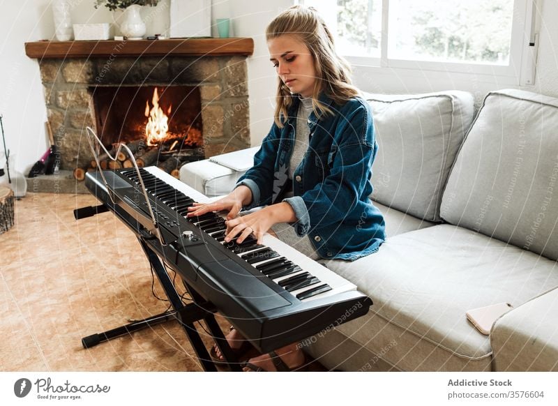Young woman playing electronic piano at home music young instrument cozy musician electric sofa composer fireplace synthesizer atmosphere relax lifestyle