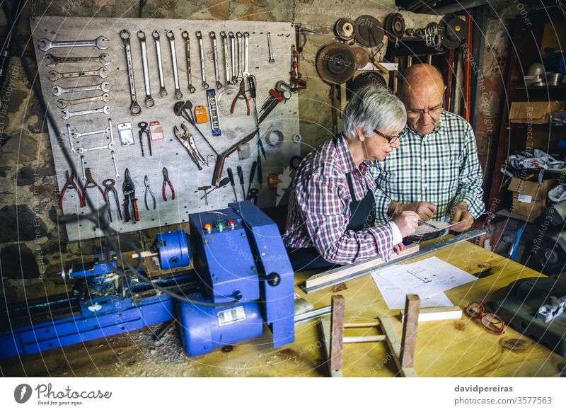 Senior couple in a carpentry carpentry shop senior working carpenter looking plans workshop wood mature machinery business caucasian home retirement worker