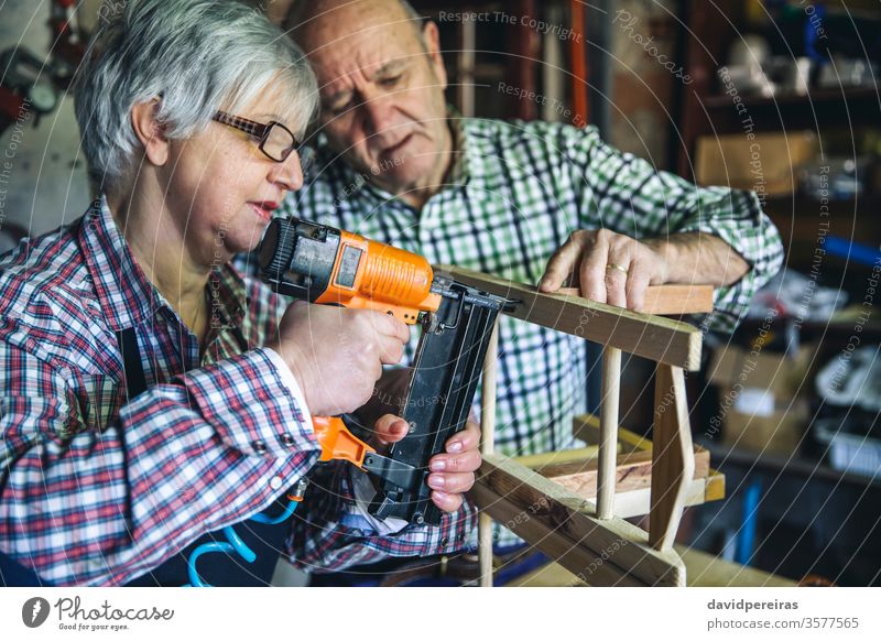Senior couple in a carpentry woman artisan staple gun nail points assembling chair diy carpenter furniture senior workshop working wood mature business