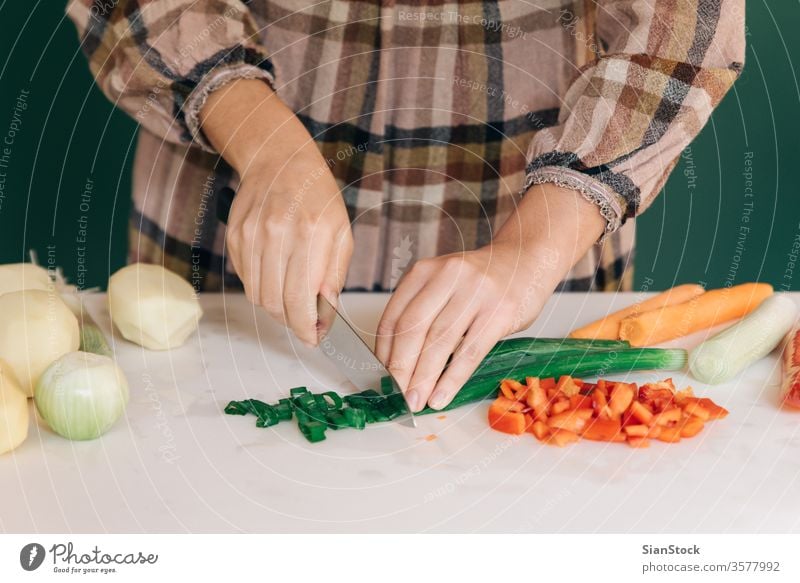 Woman cuts fresh green onion at her kitchen on white marble, to prepare her food. woman peel vegetable pepper red potatoes vegan home peel-off peeling carrots