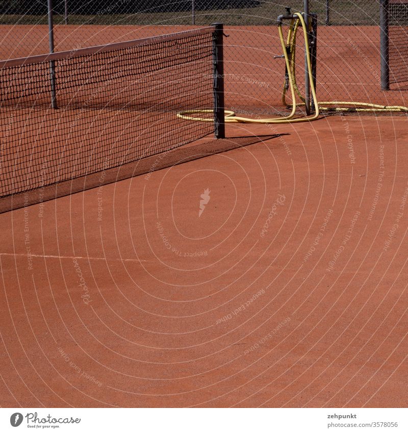 Detail of a tennis court with parts of the net, red sand, yellow water hose, narrow shadow of the net Tennis court Net Water hose Red Yellow Black Blank space