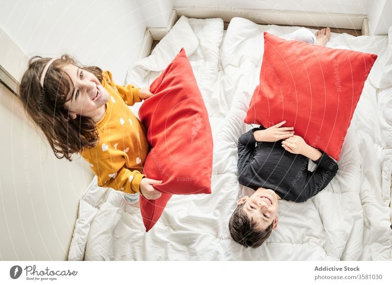 Playful siblings having pillow fight on bed home fun children blanket playful brother lounge sister having fun cozy soft together friendly childhood joy bedroom