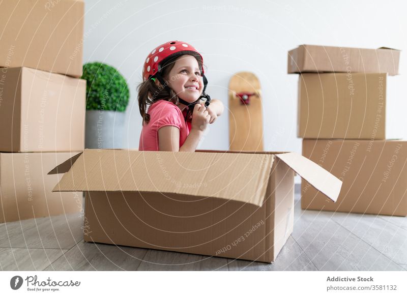 Cheerful girl playing in carton box smile helmet fasten sit moving relocate fun imagination kid child fantasy happy little cute home adorable excited glad