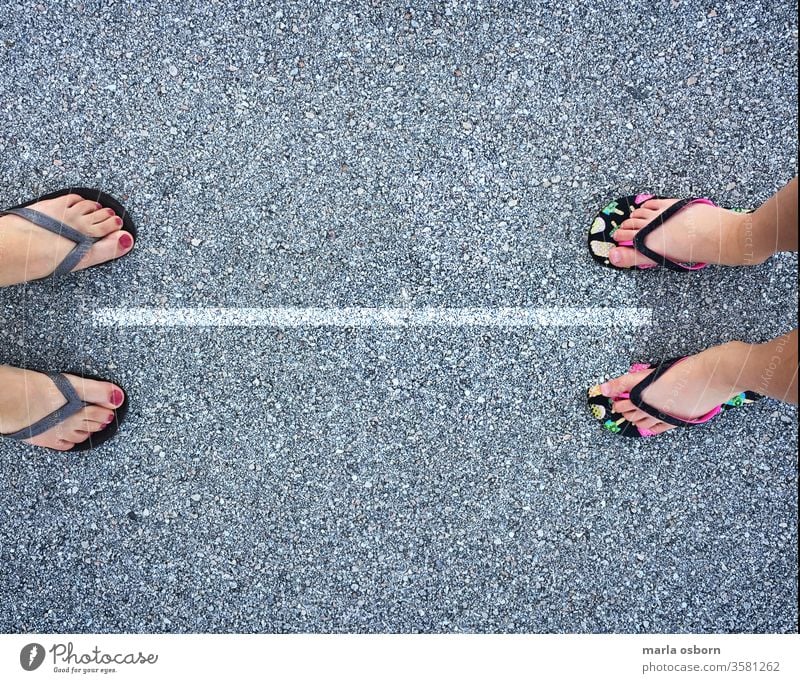 View from above of adult and child in flip flops with line separating them 6 feet apart, social distancing concept Exterior shot Protection Legs apart Nature
