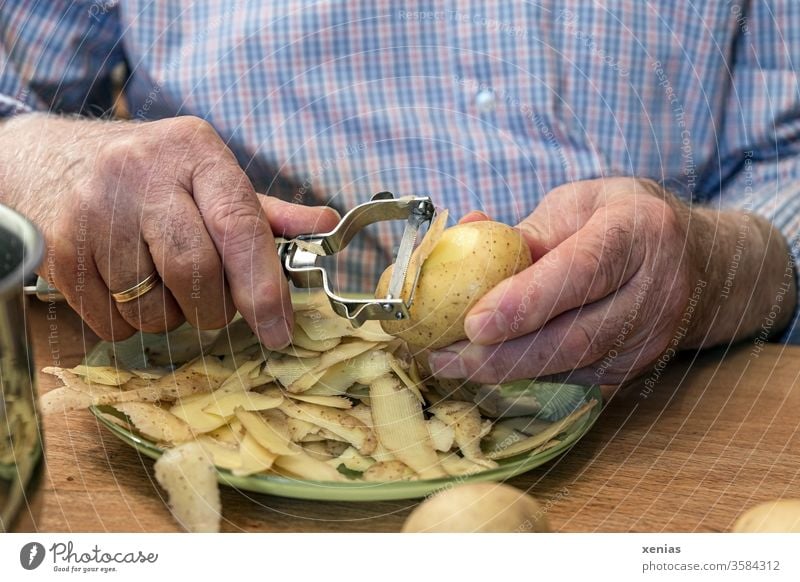 Man's hands with paring knife: senior in blue-checked shirt peels potatoes at table Senior citizen senior citizens Potatoes Peeling knife Plate Wedding band