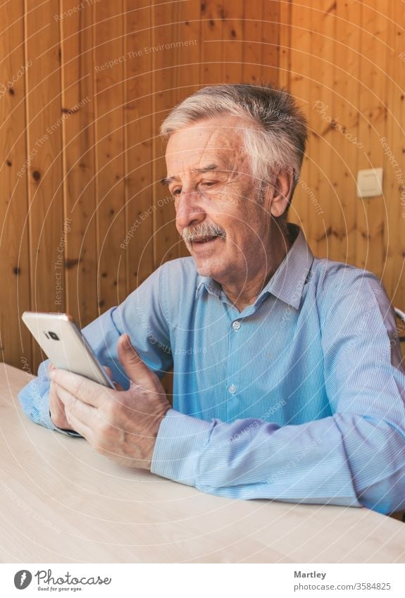 Happy gray-haired older man using a smartphone, making a video call to his  grandchildren or family at home during the coronavirus. Watching funny  videos on social networks. - a Royalty Free Stock