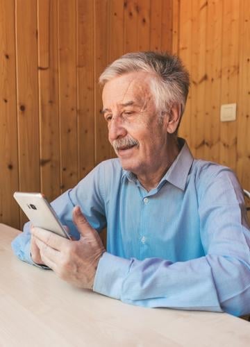 Happy gray-haired older man using a smartphone, making a video call to his grandchildren or family at home during the coronavirus. Watching funny videos on social networks.