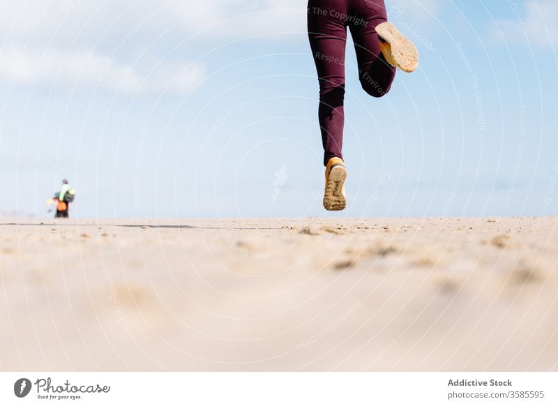 Crop content woman jumping on sandy beach carefree enjoy summer freedom relax positive dreamy female casual jeans sneakers hop style ground lady active