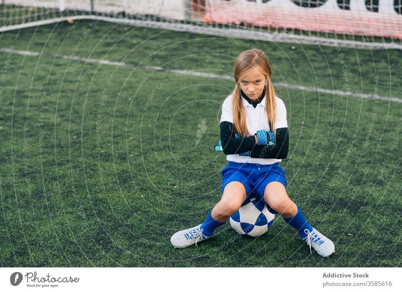 Upset young female goalkeeper sitting on ball in front of goal post on football field girl upset soccer lose frown dissatisfied failure frustrate play uniform