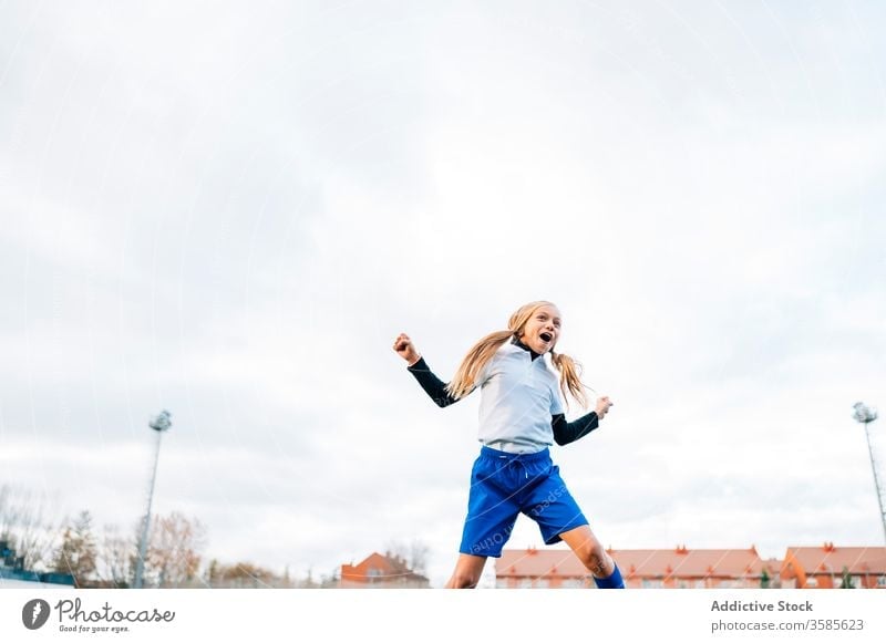 Happy young female player rejoicing in success while playing football at sports stadium girl soccer win kid celebrate goal victory happy field triumph rejoice