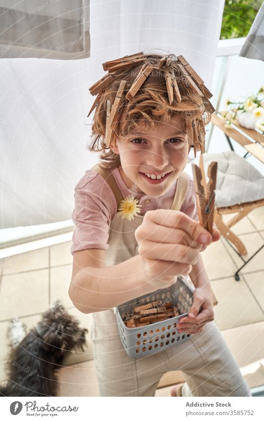 Cheerful little boy with clothes pegs attached to hair sitting on balcony home fun clothespin hairstyle pretend game happy entertain kid show leisure sun enjoy