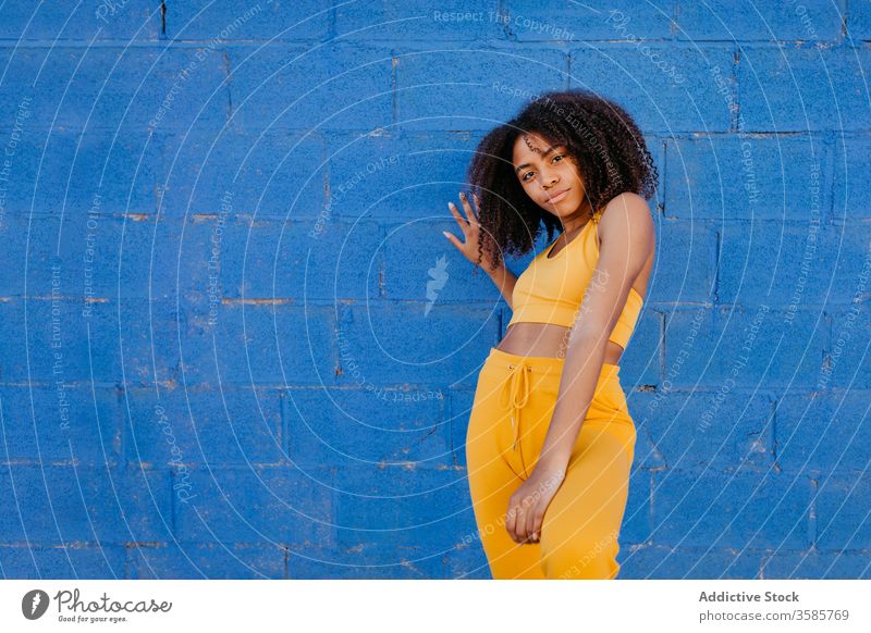 Tranquil ethnic woman with outstretched arms near blue wall afro hairstyle tranquil vivid vibrant bright female black african american city brick wall serene