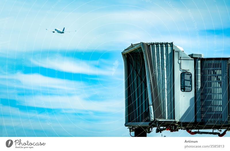 Jet bridge after commercial airline take off at the airport and the plane flying in the blue sky and white clouds. Aircraft passenger boarding bridge docked. Departure flight of international airline.