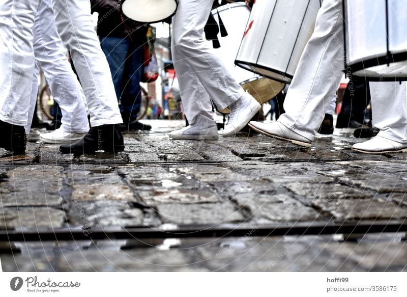 people dressed in black and white walk over cobblestones - it has rained but the train continues Legs Black White garments Going March Drum marching formation