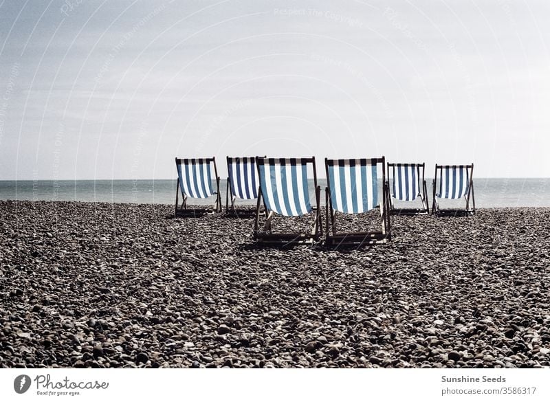 Blue striped deck chairs on a British pebble beach brighton great britain no one empty nobody rental united-kingdom coastal water peaceful seasonal blue stripes