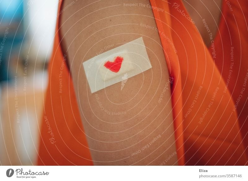 A plaster with a small red heart on it on the upper arm of a woman. Concept vaccination and care. pavement Heart Immunization Red violation concept Considerate