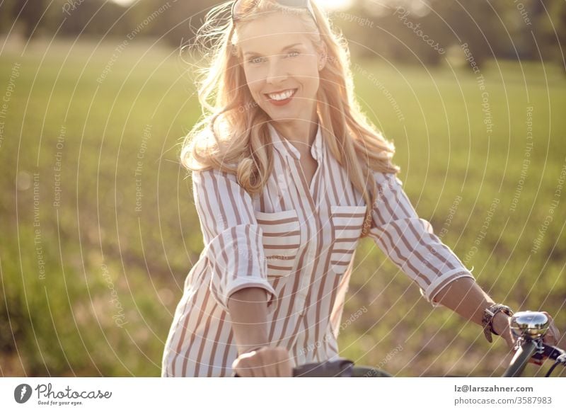 Portrait of a beautiful woman smiling happy while wearing a striped shirt and riding a bicycle in the countryside in a sunny day face portrait summer