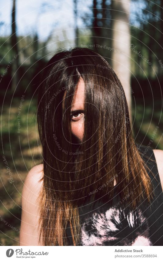 Young mysterious woman in green park expressive mystery provocative daytime summertime hair cover face stand female young long hair hide style t shirt rock