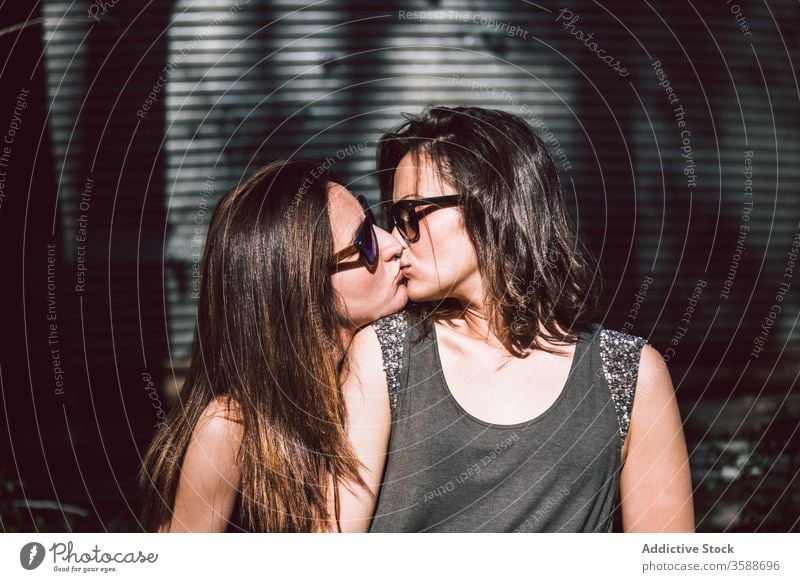 Young lesbian couple kissing on street women summer same sex summertime daytime stroll walk young tender sunglasses casual outfit homosexual lgbtq gay lifestyle