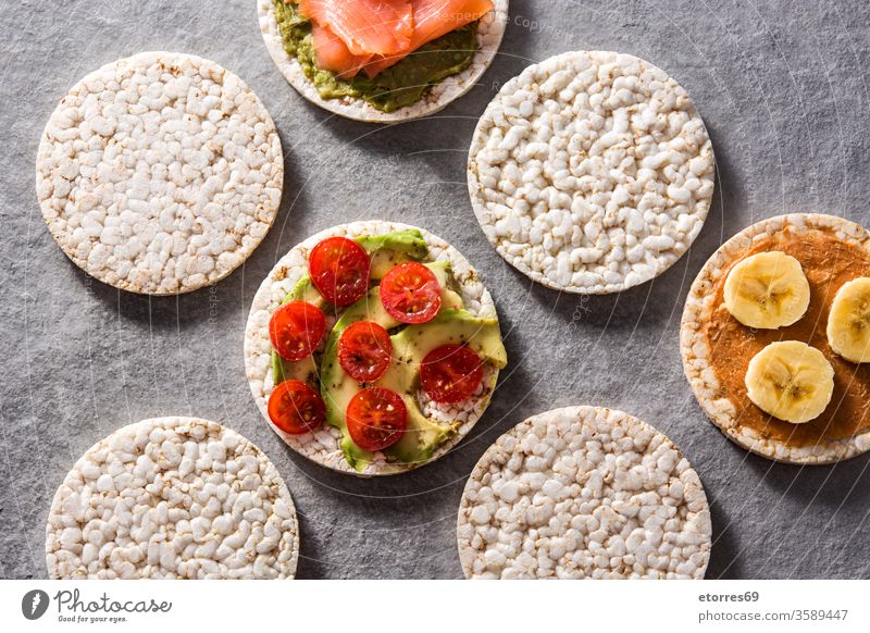 Puffed rice cakes with guacamole salmon,tomato and avocado, and banana with peanut butter on gray stone background assortment cherry cream delicious diet